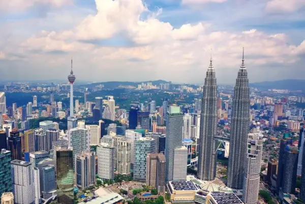 A vibrant city skyline of Malaysia featuring numerous tall buildings against a clear blue sky.