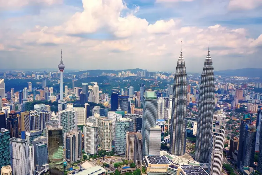 A vibrant city skyline of Malaysia featuring numerous tall buildings against a clear blue sky.
