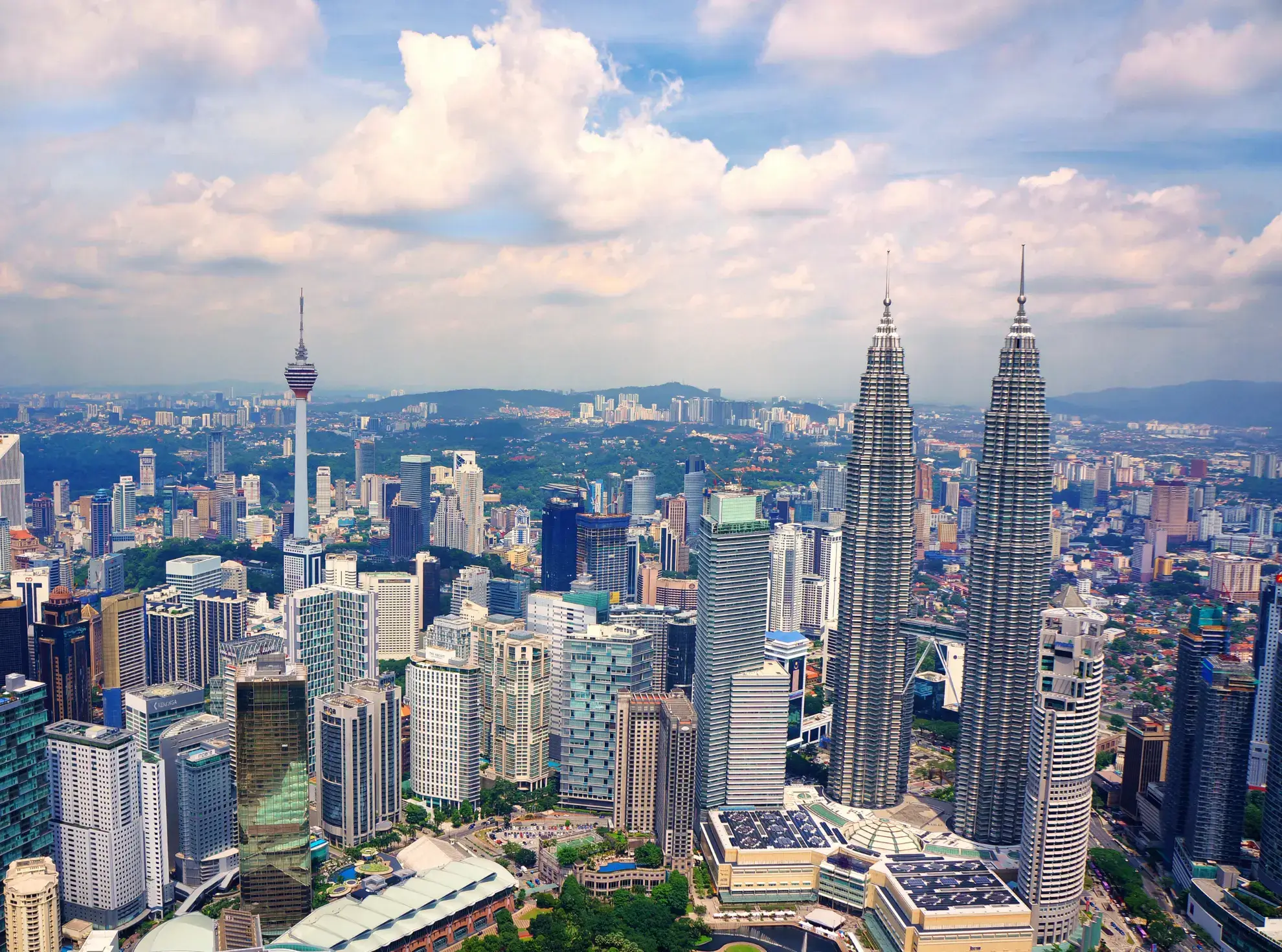 A vibrant city skyline of Malaysia featuring numerous tall buildings against a clear blue sky.